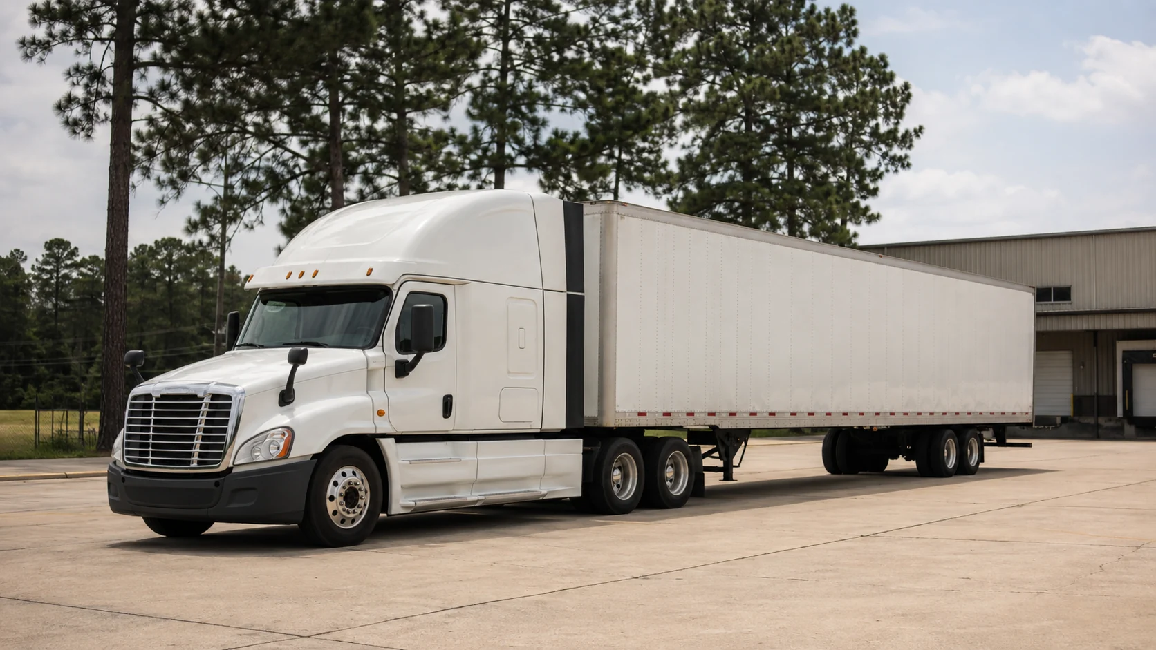 An unbranded white truck and trailer parked beside a pine-lined industrial yard in a representative Texas scene